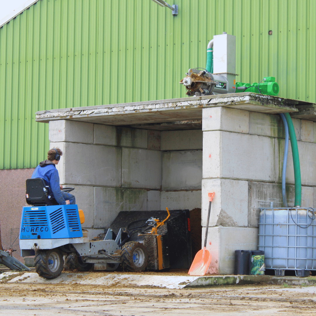 Met de instrooier het verse diepstrooisel oppakken, wat door de mestscheider op de bunker is gemaakt.