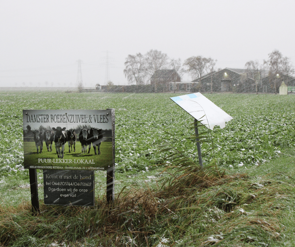 Het uithangbord van Damster Boerenzuivel en Vlees met op de achtergrond de boerderij in winterse sferen